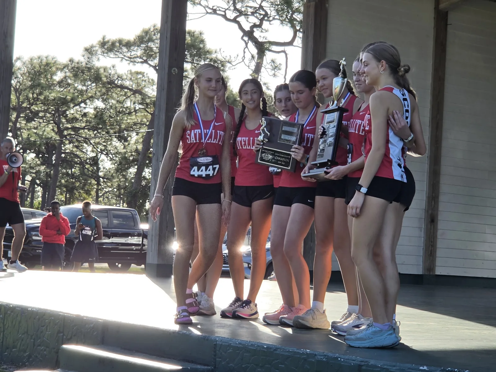 Satellite girls in red singlets on the pavilion stage at Wickham Park holding the Cape Coast Conference trophy and plaque during the awards