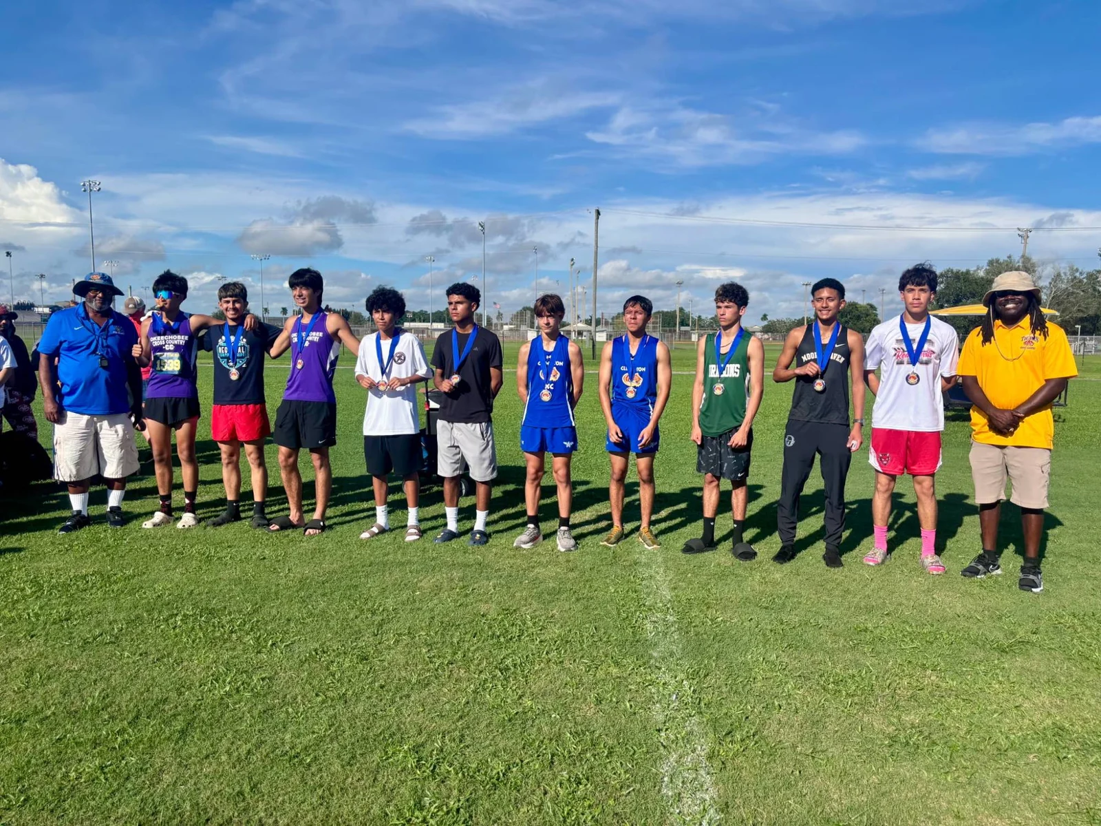 The boys' medalists at the Clewiston XC Sugar Run Invite lined up with their medals between two meet officials
