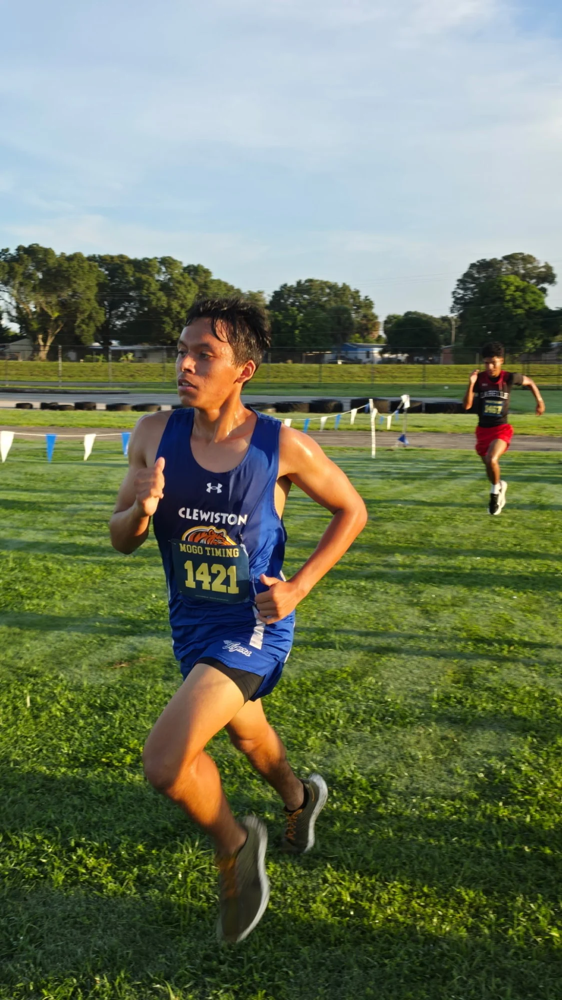 A Clewiston runner in a blue singlet, bib 1421, with a LaBelle runner behind him