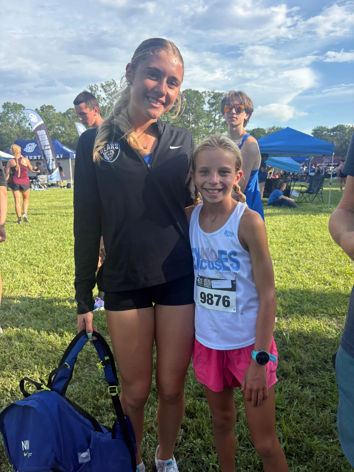 Colette Heffernan of No Excuses Running Club in her race bib standing with Avery Hartley of Bartram Trail at a cross country meet