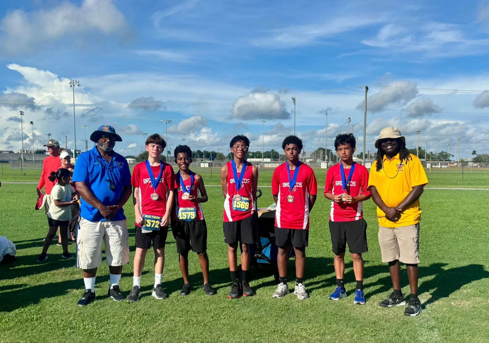 Five LaBelle Middle School boys in red Broncos shirts with medals, between two meet officials