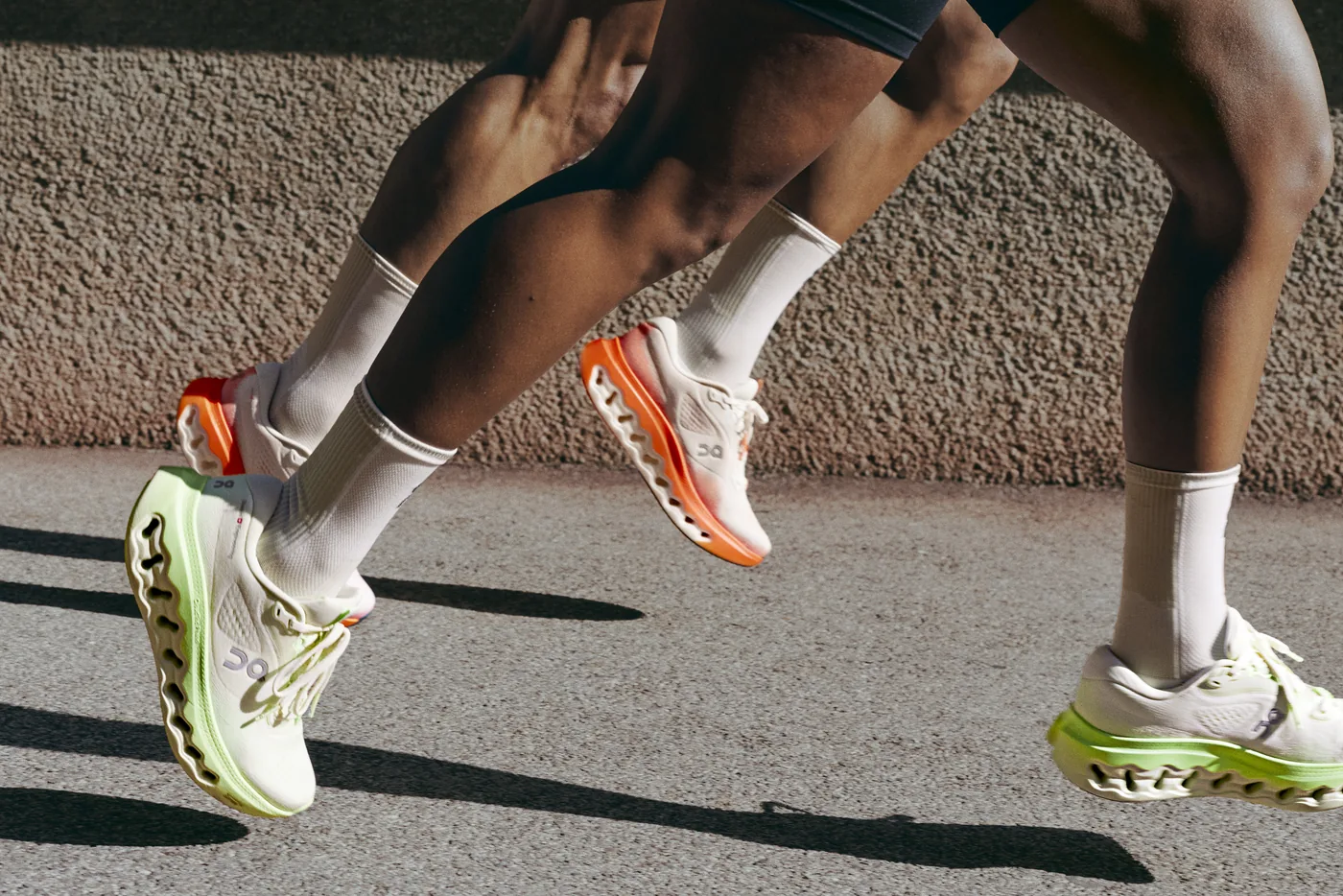 Two runners on pavement wearing On Cloudsurfer 3 shoes in white with lime and orange accents