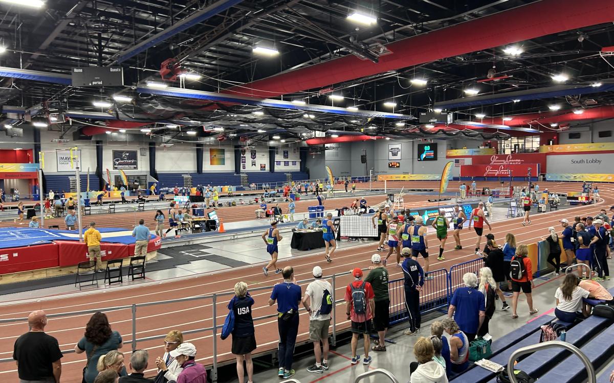 Runners race around the banked 200m indoor track at the Alachua County Sports and Events Center during the 2025 World Masters Athletics Indoor Championships, with spectators along the rail