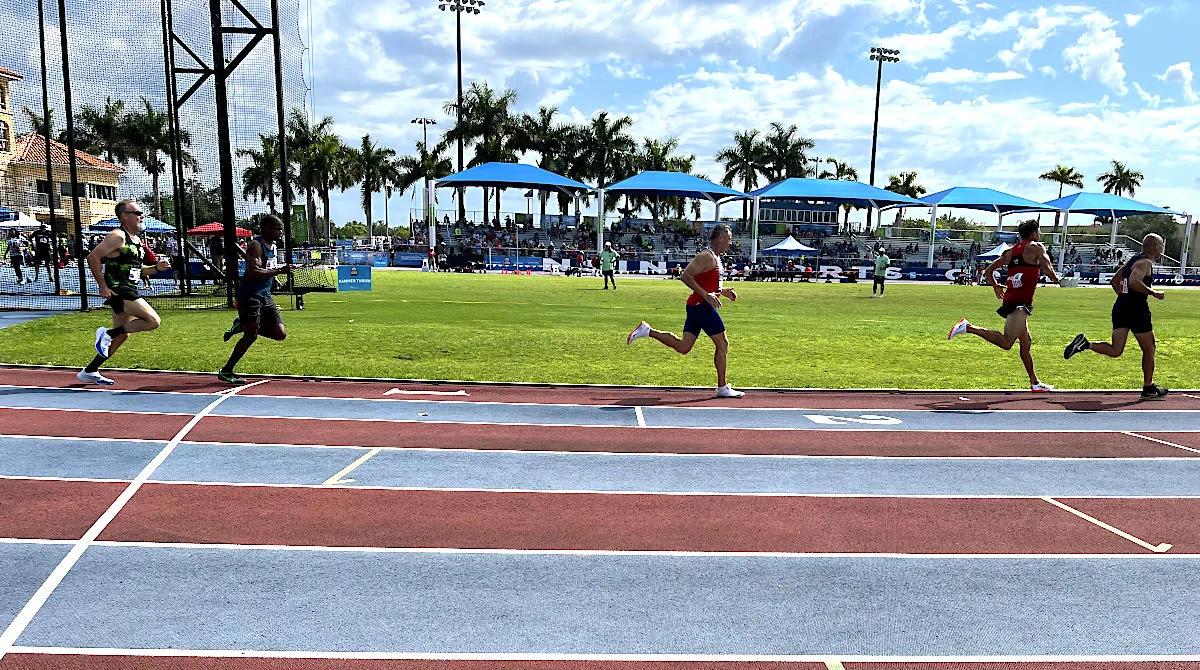 Masters runners racing the 800 meters on the Ansin Sports Complex track in Miramar, with shaded grandstands behind